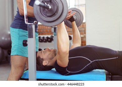 Unidentifiable Spotter Helping Bearded Man In Black Shirt And Pants Perform Bench Presses In Gym