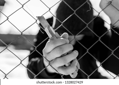 Unidentifiable Teenage Boy Behind Wired Fence Holding A Paper Knife At Correctional Institute, Focus On The Boys Hand, Conceptual Image Of Juvenile Delinquency.