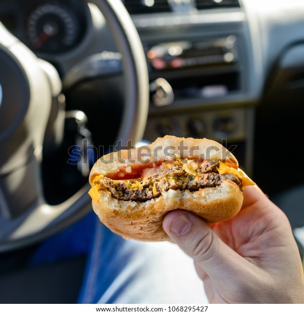Unidentified man eating a burger while driving a\
car, close-up