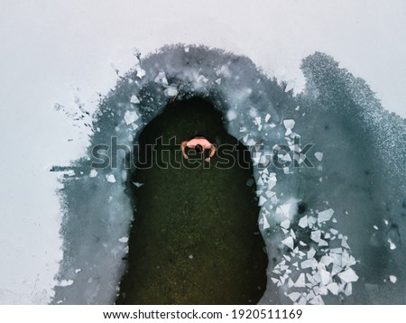 Unidentified man in a lake, in ice-hole of icy water covered with white snow and ice