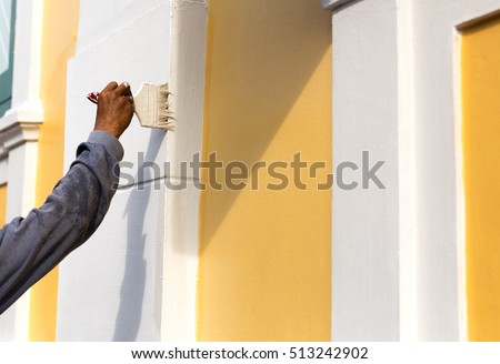 Unidentified man painting with brush on the building wall outside