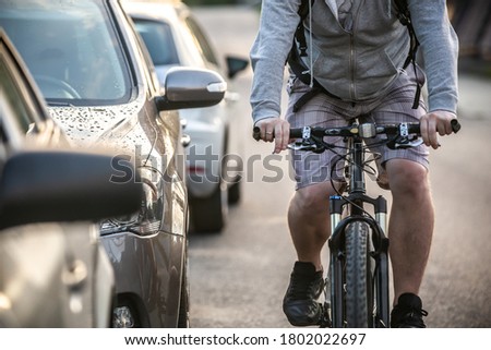 An unidentified man riding a bicycle passing cars on the road in the traffic. A cyclist overtaking cars with high speed.