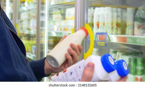 An Unidentified Man In A Store Selects Products At The Dairy Counter, Reads The Composition And Checks The Expiration Date, And Then Puts The Purchases In A Basket For Payment At The Checkout.