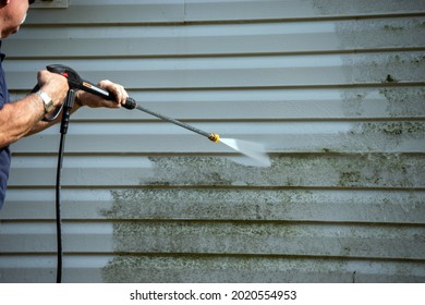 An unidentified man uses a power washer to clean mold and grime off the siding of a house.