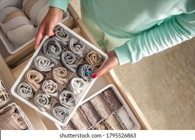 Unidentified neat housewife puts container with socks and pantyhose on wardrobe drawer during general cleaning by modern storage system. Concept of beautiful and comfortable organization