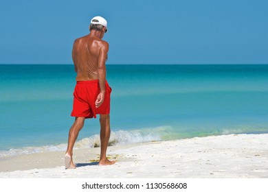 Unidentified Older Man Walking On The Beach Getting Exercise And Enjoying A Beautiful Sunny Day. 