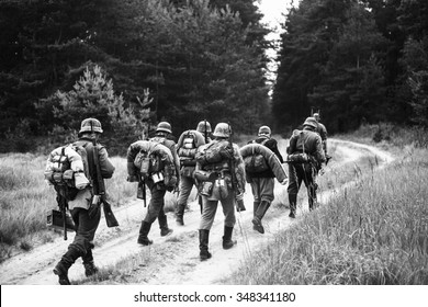 Unidentified re-enactors dressed as World War II German soldiers walks  on forest road. Black and white photography