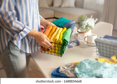 Unidentified woman in casual clothes lays clothes in metal mesh container in rainbow order on a table with a tray with a flower. Lady fly and clean house concept