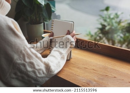 Unidentified woman is writing in the notepad in cafe. Working on bullet journal, diary, morning pages, plans and goals. Copy space for your text.