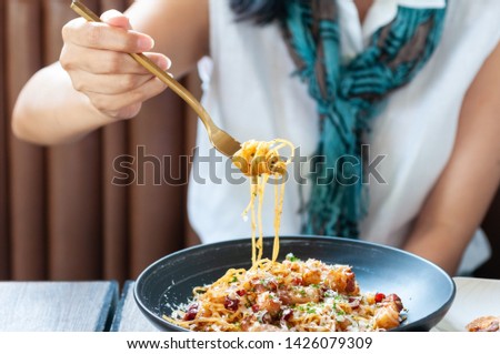 Unidentified young Asian woman use gold fork lift up spaghetti noodle show to camera, spicy spaghetti with bacon mix together.