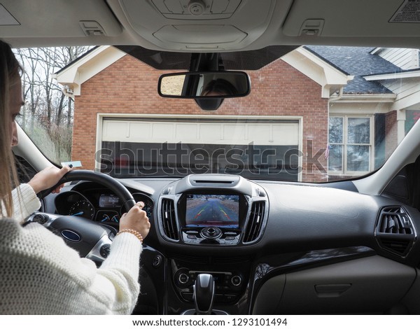 Unidentified\
young lady is reversing the car from garage on the drive way using\
rear camera while looking at the\
screen.