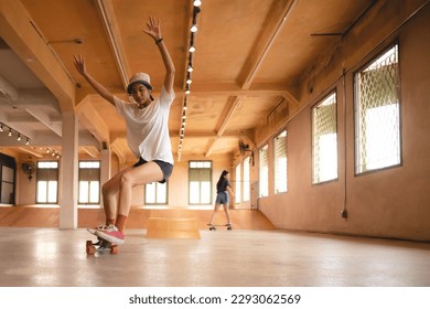 Unidentified young woman in casual sports clothing learning and practicing skateboarding while trying to balance with arms extended on artificial indoor small slide in skating studio during daytime - Powered by Shutterstock