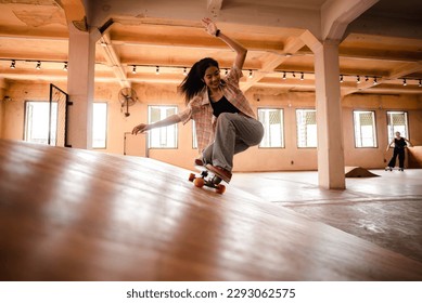 Unidentified young woman in casual sports clothing learning and practicing skateboarding while trying to balance with arms extended on artificial indoor small slide in skating studio during daytime - Powered by Shutterstock