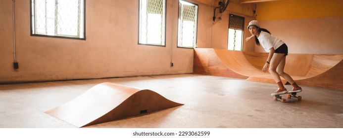 Unidentified young woman in casual sports clothing learning and practicing skateboarding while trying to balance with arms extended on artificial indoor small slide in skating studio during daytime - Powered by Shutterstock