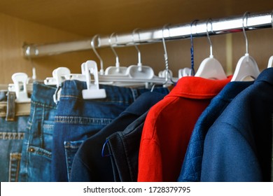 Uniform Blue Clothes For A Teenage Boy Hanging In A Closet On Different Hangers. One T-shirt Is Red. The Concept Is The Uniformity Of Clothes.