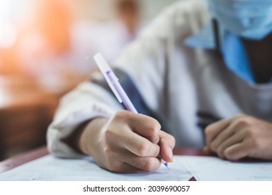 Uniform Student Taking Exam While Wearing Face Mask Due To Coronavirus Emergency. Young Woman Sitting In Class With Wearing Surgical Mask Due To Covid-19 Pandemic