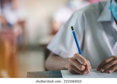 Uniform Student Taking Exam While Wearing Face Mask Due To Coronavirus Emergency. Young Woman Sitting In Class With Wearing Surgical Mask Due To Covid-19 Pandemic