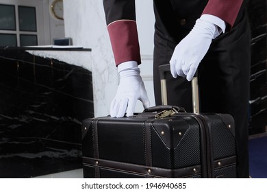 A Uniformed Doorman Holds A Brown Leather Suitcase In His Hand. The Hands Of The Doorman In White Cotton Gloves.Hotel Service .The Holiday Season.An Unrecognizable Person