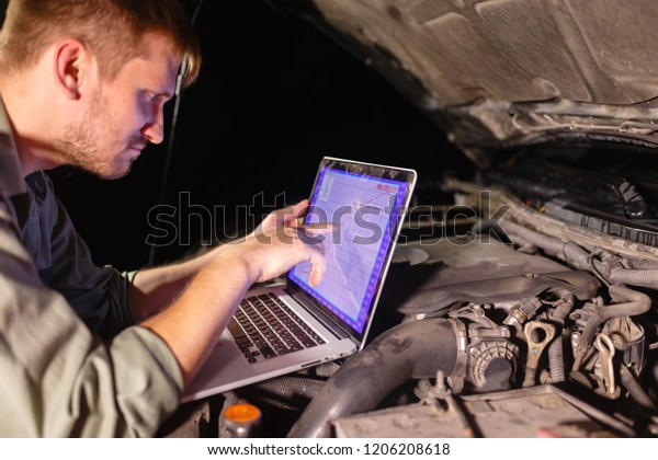 The uniformed mechanic looks intently at the\
laptop and points his finger at the horsepower and torque graph.\
Mechanic carries out maintenance of the car. The removal of bugs of\
the engine.