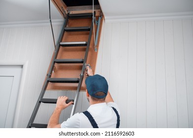 a uniformed specialist fixes a metal ladder to the hatch of the attic door. - Shutterstock ID 2116592603