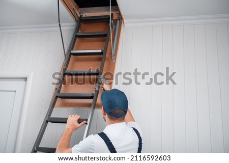 a uniformed specialist fixes a metal ladder to the hatch of the attic door.