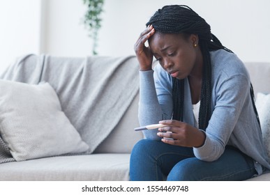 Unintended pregnancy. Depressed african american woman upset with positive test results, sitting on couch at home with sad face expression