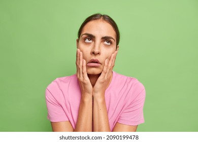 Uninterested bored young woman keeps hands on cheeks fed up of dull conversation looks above makes facepalm and rolls eyes hears nonsense wears casual t shirt isolated over green background. - Shutterstock ID 2090199478
