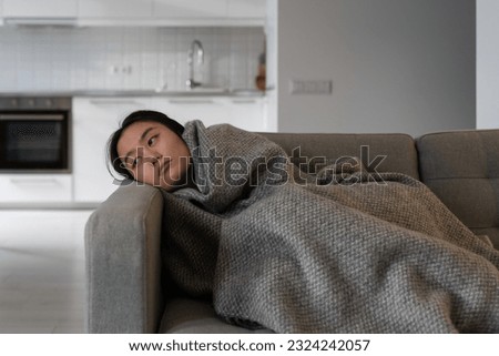Uninterested tired Asian Korean young woman sadly looking away in bad mood lies on couch under wool blanket at home thinks about problems suffering depression in mental health, burnout or broken heart Imagine de stoc © 