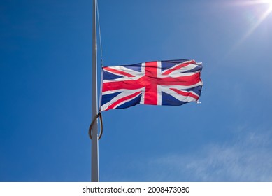 Union Jack flag flying at half mast against blue sky and sun. - Shutterstock ID 2008473080
