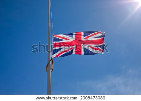 Union Jack flag flying at half mast against blue sky and sun.