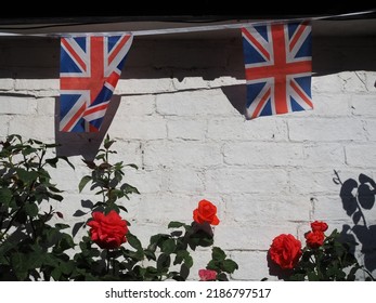 Union Jack UK Flag Bunting With Red Roses And Painted White Wall Background.