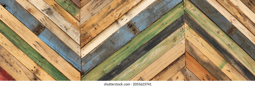 unique abstract geometric patterns made from recycled natural cut timber palettes arranged in diagonal stripes. Multi colored textural upcycled planks of wooden parquetry in a herringbone format. 