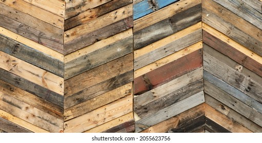 unique abstract geometric patterns made from recycled natural cut timber palettes arranged in diagonal stripes. Multi colored textural upcycled planks of wooden parquetry in a herringbone format. 