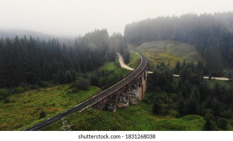 Unique arched viaduct bridge in the Carpathians. Green hills covered with light haze.