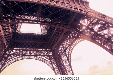 A unique architectural perspective of the Eiffel Tower in Paris, captured from underneath its sweeping iron arches. The interplay of light and shadow reveals the intricate design of this monument.