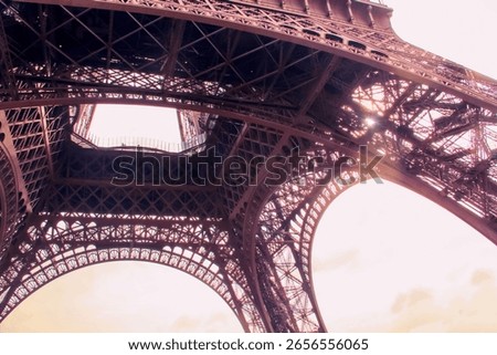 A unique architectural perspective of the Eiffel Tower in Paris, captured from underneath its sweeping iron arches. The interplay of light and shadow reveals the intricate design of this monument.