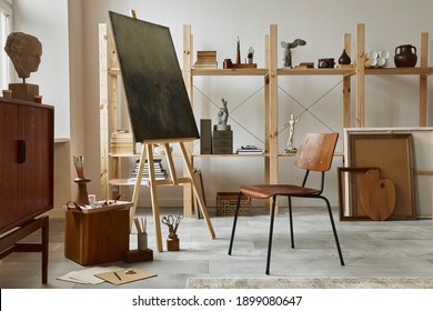 Unique artist workspace interior with stylish teak commode, wooden easel, bookcase, artworks, painting accessories, decoration and elegant personal stuff. Modern work room for artist. Template.