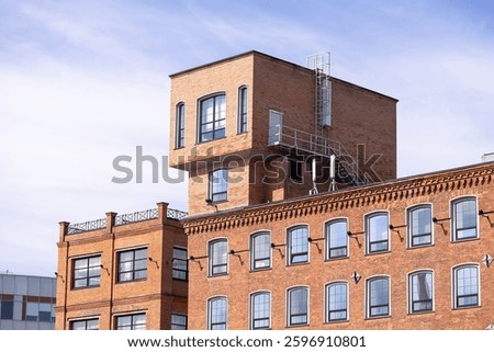 Unique brick building with an elevated modern loft extension, featuring large windows and external stairs, against a bright sky. Urban architecture concept