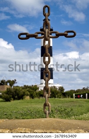 Unique composition of a cross made from welded anchor chain links standing in front of the Phare de Chassiron lighthouse