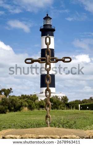 Unique composition of a cross made from welded anchor chain links standing in front of the Phare de Chassiron lighthouse