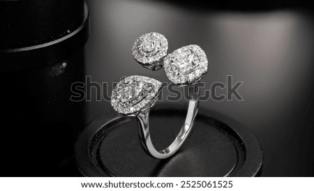 A unique diamond ring featuring three stones, a pear-shaped diamond flanked by two square-cut diamonds, set in a gleaming white gold band. The ring is displayed on a black velvet cushion, highlighting