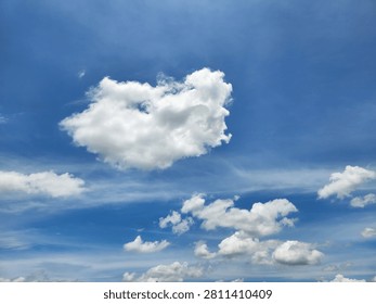 Unique heart-shaped white cloud floating in a clear blue sky above smaller scattered clouds.