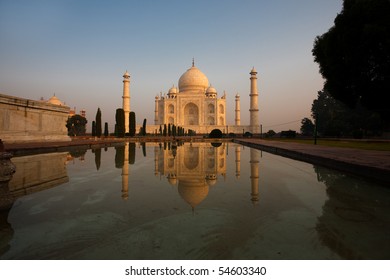 Unique image of front facade of Taj Mahal reflected in the side central water fountain while glowing with colorful morning sunrise red in Agra, India. Horizontal copy space