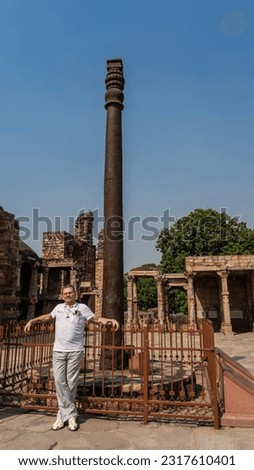A unique iron pillar that does not rust is located in the ancient Qutub Minar temple complex. A man stands at the fence. Ruins in the distance. Blue sky. India. Delhi.