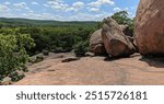 In the unique landscape of Elephant Rocks, Missouri, hikers make their way among large, smooth boulders weathered into shapes that evoke elephant silhouettes, all under a bright, open sky.