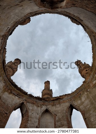 A unique low-angle shot looking up through the circular opening of a collapsed dome in the ruins of Novomalyn Castle. The brick walls and arched windows frame a cloudy sky, showcasing the ancient architectural heritage.