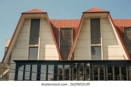 Unique modern building facade with triangular roof design and glass windows under clear blue sky. Architectural exterior shot in daylight.