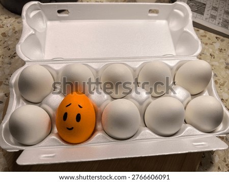 Unique orange egg with smiling face in white carton box, leadership and standing out from the crowd concept