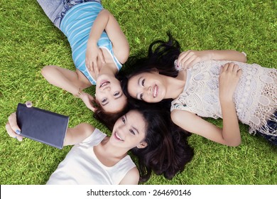 Unique Perspective Of Beautiful Teenage Girls Lying Down On Grass While Taking Self Portrait With Cellphone At Field