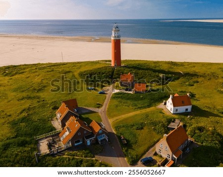 A unique perspective drone view at the lighthouse standing tall on a sandy beach, against a backdrop of the ocean waves crashing. The iconic red lighthouse of Texel Netherlands at sunset